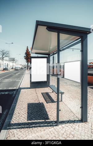 Zwei leere Werbe- und Informationstemplaten in einer modernen Glasbuswartehalle, die eine vertikale Plakatwand und eine seitliche Kartenleiste neben einem sonnigen U zeigen Stockfoto