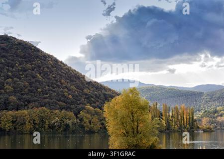 Wunderschöne Herbstlandschaft des Lago di Piediluco in Terni, Umbrien, Italien, mit farbenfrohen gelben Bäumen und bewaldeten Hügeln unter einer dramatischen Wolkenformation Stockfoto