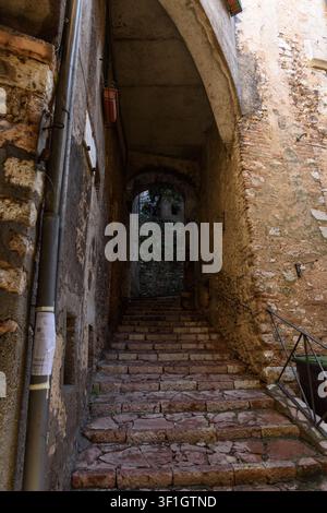 Vertikale Aufnahme einer mittelalterlichen Steintreppe, die durch einen historischen gewölbten Durchgang mit verwitterten Ziegelwänden in der Hügelstadt Stroncone aufsteigt, U Stockfoto