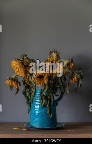 Welke Sonnenblumen in einer blauen Keramikvase Stillleben auf Holztable mit stimmungsvoller Beleuchtung Stockfoto