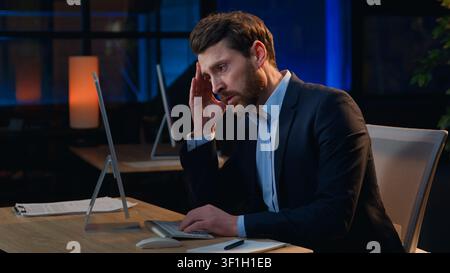 Müder, erschöpfter kaukasischer Geschäftsmann mittleren Alters mit Computer fühlt sich erschöpft, Stressproblem, Burnout im Nachtbüro, überlasteter Geschäftsmann Stockfoto