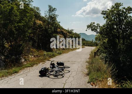 Beladenes Gravel-Fahrrad, das während einer Bikepacking-Reise auf einer ruhigen Bergstraße in Montenegro ruht. Die malerische Route windet sich durch Wälder und felsiges Gelände Stockfoto