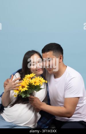 Glücklicher Ehemann umarmt seine schwangere Frau, die einen Sonnenblumenstrauß hält Stockfoto