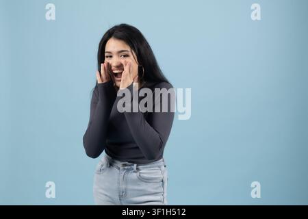 Junge Frau, die sich mit der Hand über den Mund bedeckt und über eine lustige Geschichte lacht Stockfoto