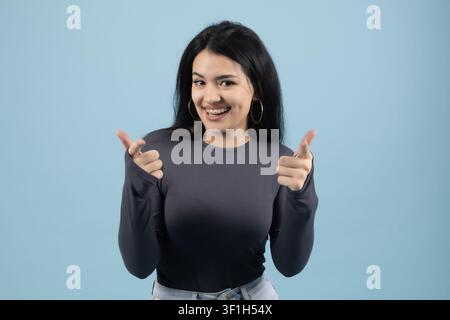 Glückliche junge Frau zeigt mit beiden Händen Daumen hoch und lächelt Stockfoto