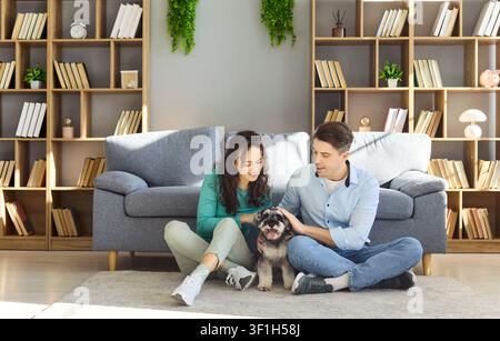 Glückliches Paar sitzt zu Hause auf dem Boden und kuschelt mit einem Mini-Schnauzer-Hund im Wohnzimmer Stockfoto