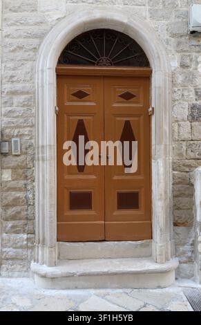 Alte hölzerne Doppeltür mit geschnitzten Diamantpaneelen und Schmiedeeisen-Details, eingebettet in einen Steinbogen in einer historischen Gebäudefassade. Italien, Apulien Stockfoto