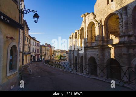Eine malerische Straßenszene in Arles, Frankreich, mit dem historischen römischen Amphitheater, das in Sonnenlicht getaucht ist, und bezaubernden alten Gebäuden, die die Straße säumen Stockfoto