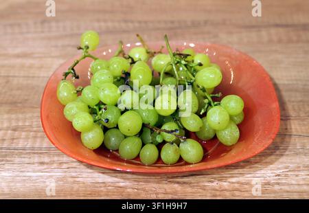 Frische grüne Trauben sind reichlich auf einem orangefarbenen Teller aus Glas vorhanden, der auf einem Holztisch steht, und bieten einen gesunden und süßen Snack, der einen natürlichen Überfluss darstellt Stockfoto