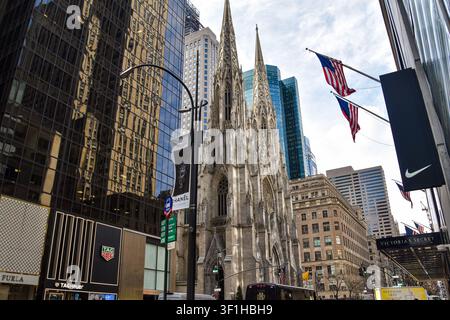 St. Patrick's Cathedral an der Fifth Avenue, eingerahmt von modernen Wolkenkratzern, amerikanischen Flaggen und Luxus-Einzelhandelsgeschäften in Midtown Manhattan, New York City, USA. Stockfoto