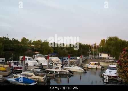 Zahllose Freizeitboote und Yachten, die entlang eines Holzstegs in einer Marina an einem ruhigen Fluss vertäut sind, gesäumt von üppigen grünen Bäumen unter einem Himmel der goldenen Stunde. Stockfoto