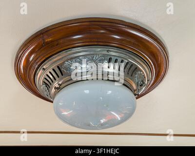 Luxuriöses Vintage-Zuginterieur, Deckenleuchte, kreisförmiger Holzrahmen, metallischer dekorativer Ring, mattierter Glasglobus, warme Brauntöne, aus Stockfoto
