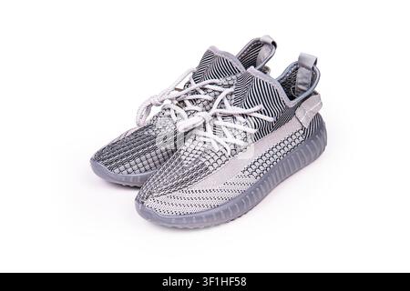 Moderne sportliche Turnschuhe in neutralem Grauton, mit gestricktem Obermaterial, weißen Schnürsenkeln, durchscheinender Zwischensohle, gerippter Außensohle, dynamischer Winkelkomposition, Mini Stockfoto
