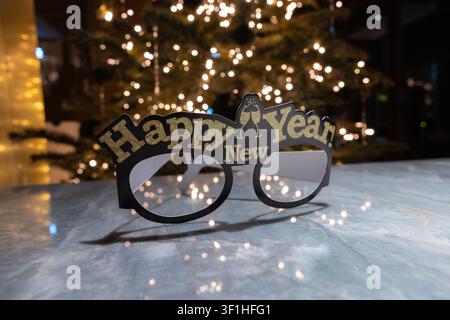 "Frohes neues Jahr" Papp-Partygläser mit goldglitzerndem Text auf einer Marmoroberfläche mit einem unscharfen Weihnachtsbaumhintergrund. Stockfoto