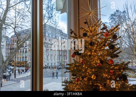 Hell erleuchteter und geschmückter Weihnachtsbaum neben einem großen Fenster mit Blick auf eine Straße der Stadt. Stockfoto