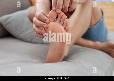 Mann massiert seinen Fuß auf dem Sofa zu Hause, Nahaufnahme Stockfoto