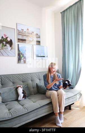 Zufriedene Frau hält eine Digitalkamera zu Hause und betrachtet aufgenommene Fotos in einem gemütlichen und modernen Interieur Stockfoto