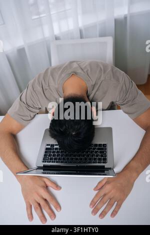 Vertikale Draufsicht auf erschöpften Freiberufler, der Burnout und Stress verspürt, liegt schlafend mit dem Gesicht auf dem Laptop nach langen Arbeitsstunden, erlebt Stockfoto