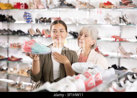 Zwei positive Frauen unterschiedlichen Alters wählen gemeinsam neue Sneaker im Modegeschäft Stockfoto