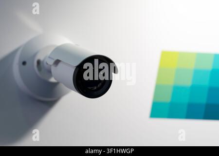 Weiße Kugel-Überwachungskamera, montiert an einer Anzeigewand neben einem farbigen Testdiagramm, schräger Blick auf Überwachungsausrüstung. Stockfoto