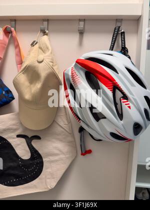 Fahrradhelm, der an Haken an der Eingangswand hängt, mit Baseballkappe Stockfoto
