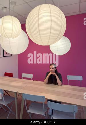 Junge Frau sitzt an einem Tisch in einem modernen rosa Café oder kreativem Arbeitsbereich Stockfoto