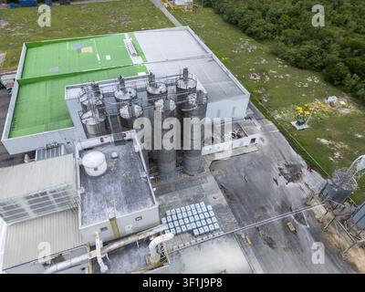Luftaufnahme einer Industrieanlage mit hohen Metall-Lagersilos, einem großen Gebäude mit einem grünen Dachteil und einem asphaltierten Hof in Mérida, Yucatán Stockfoto