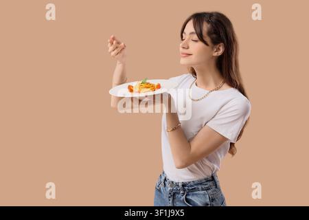 Junge Frau genießt den Duft von frisch gekochten Spaghetti mit Kirschtomaten und Basilikum auf einem weißen Teller, Freude und Zufriedenheit mit dem Essen, culi Stockfoto