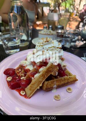Belgische Waffeln mit Erdbeeren und Sahne auf einem rosa Teller an einem Tisch in einem Café. Stockfoto