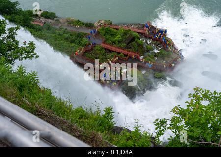 Eine Hochwinkel-Horizontalaufnahme, die auf Menschenmassen von Touristen hinunterblickt, die gelbe und blaue Regenponchos tragen, auf hölzernen Beobachtungsplattformen und Gehwegen am t Stockfoto