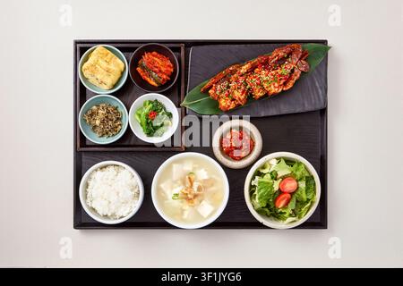 Koreanisches Setgericht Hansik mit gegrilltem Fisch oder Bulgogi, serviert auf einem schwarzen Tablett mit verschiedenen Beilagen Banchan, darunter Reis, Suppe, Kimchi und Gemüse Stockfoto