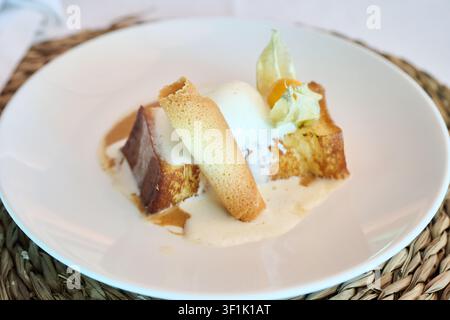 French Toast präsentiert ein köstliches Dessert, garniert mit reichhaltigem Vanilleeis, Karamellsoße, einem knusprigen Tuile-Biskuit und einer lebendigen Kapstachelbeere Stockfoto