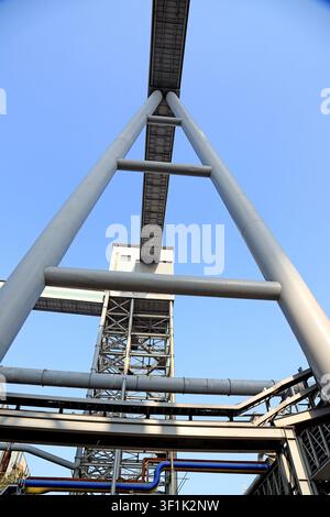 Diese hochdetaillierte, realistische Fotografie fängt eine dramatische Tiefenperspektive eines symmetrischen A-Frame-Förderturms in einem aktiven Stahlwerk ein, Rahm Stockfoto