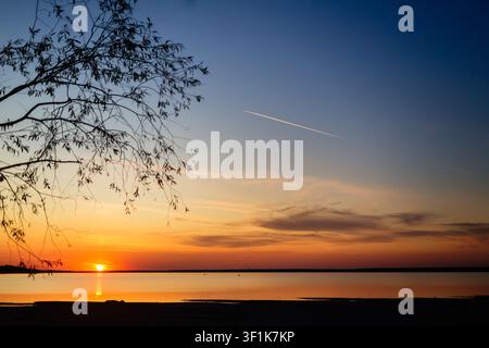 Blick auf den Sonnenuntergang durch die Äste der Weide bei einem hellen Sonnenuntergang über dem See. Ein wunderbarer Ort der Kraft und Energie. Stockfoto