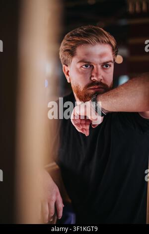 Nachdenklicher bärtiger Mann, der seine Uhr überprüft, in einem stimmungsvollen Innenporträt mit nachdenklichem Ausdruck Stockfoto