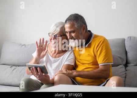 Fröhliches Seniorenehepaar, das zusammen auf dem Sofa sitzt und einen Videoanruf auf einem Smartphone tätigt. Stockfoto