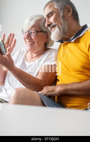 Fröhliches Seniorenehepaar, das zusammen auf dem Sofa sitzt und einen Videoanruf auf einem Smartphone tätigt. Stockfoto