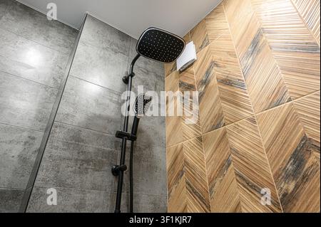 Modernes Badezimmer mit grauen und holzmustrigen gefliesten Wänden und einer schlanken schwarzen Duscharmatur Stockfoto