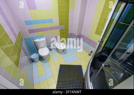 Farbenfrohes gefliestes Badezimmer mit Toilette, Bidet, Dusche und einem schwarzen Badvorleger Stockfoto