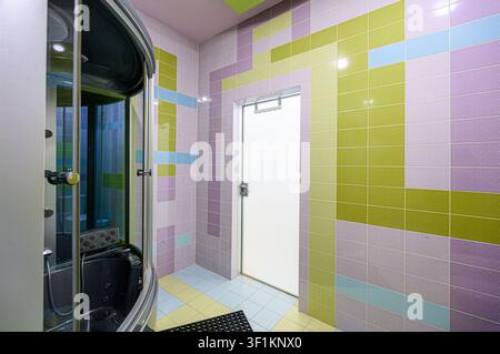 lebendiges Badezimmer mit einer Dusche, geflieste Wände in Schattierungen von Lila, Grün und Blau, mit einer Tür Stockfoto