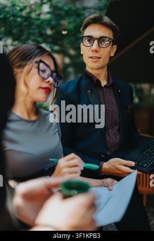 Junge Berufstätige führen ein Geschäftstreffen im Freien und prüfen Dokumente mit einem Laptop Stockfoto
