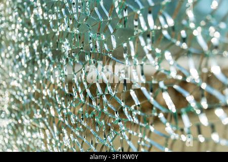 Nahaufnahme von zersplittertem Hartglas mit Spinnennetz-Rissen und Lichtreflexionen. Ideal für Sicherheits- und Versicherungskonzepte Stockfoto