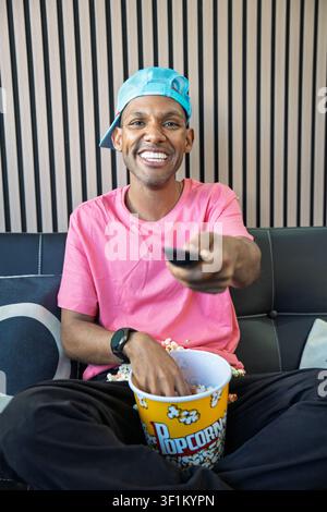 Junger Mann lächelt, entspannt zu Hause, schaut fern und genießt Popcorn Stockfoto