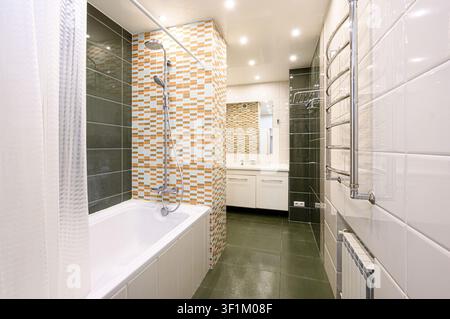 Modernes Badezimmer mit einer weißen Wanne, Dusche, bunten Mosaikfliesen und einem eleganten Waschtisch. Der Raum zeichnet sich durch neutrale Töne und helle Beleuchtung aus Stockfoto