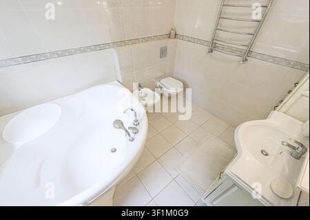 helles, gefliestes Badezimmer mit einer Whirlwanne, Toilette, Bidet und einem Handtuchhalter Stockfoto