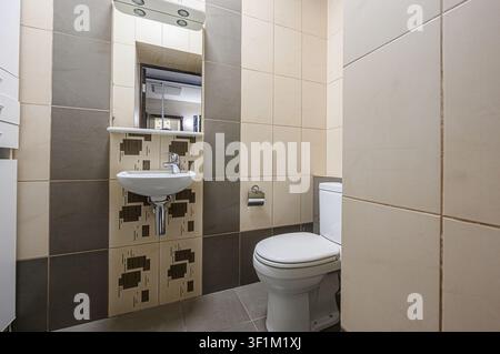 Badezimmer verfügt über eine weiße Toilette, ein Waschbecken mit gemusterter Rückwand und Fliesen in neutralen Tönen Stockfoto