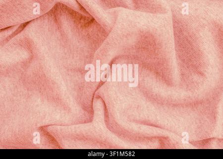 Horizontale Nahaufnahme eines weichen pastellrosa gestrickten Baumwollstoffmaterials mit unordentlichen Falten und Knittern auf einer gemütlichen, bequemen Decke Stockfoto