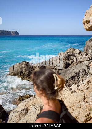 Frau mit Rucksack, die das türkisblaue Meer in der Bucht von Coll Baix auf Mallorca betrachtet Stockfoto