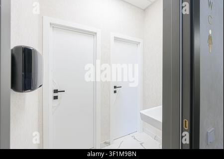 heller Toilettenbereich mit zwei weißen Türen, einem schwarzen Handtrockner und einem Damen-WC-Schild Stockfoto