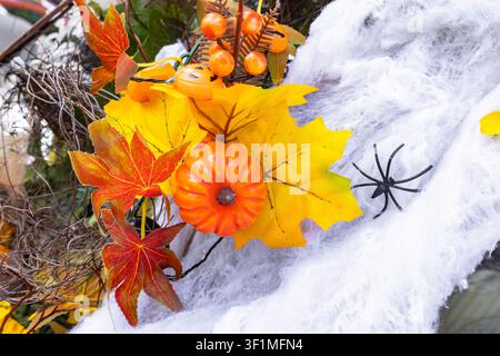 Halloween-Dekoration-Kranz mit künstlichen orangefarbenen Kürbissen, Herbstblättern und einer schwarzen Spinne auf weißem Netz Stockfoto